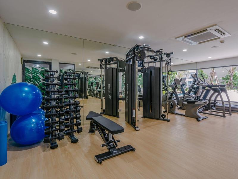 Moderner Fitnessraum mit Hanteln, Trainingsgeräten und großen Fenstern mit Blick ins Grüne.