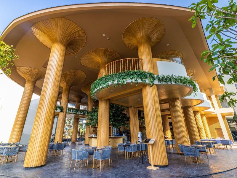 Außenbereich eines Restaurants mit dicken, goldfarbenen Säulen und blauen Sitzgelegenheiten unter einem gewölbten Dach.