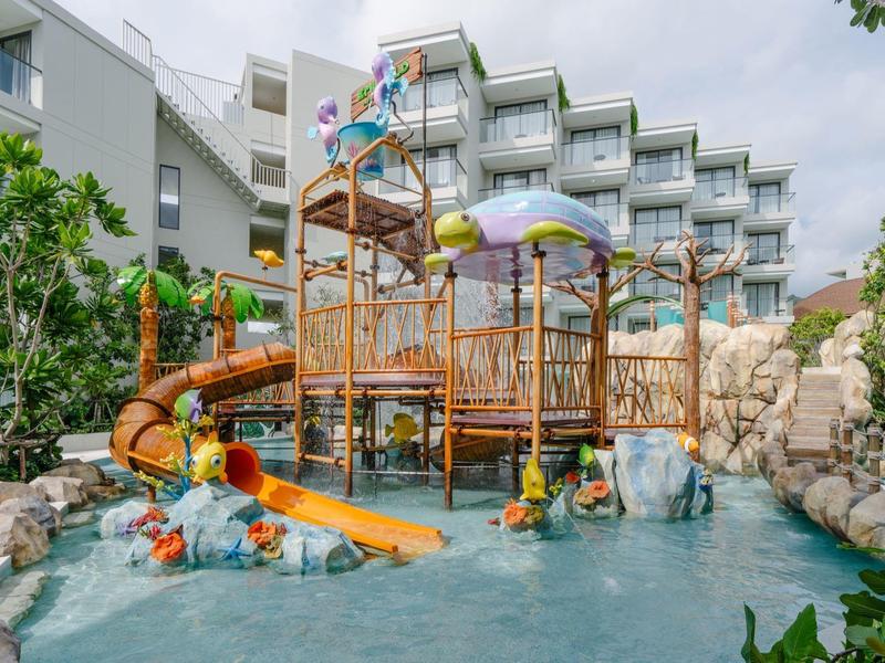 Wasserpark mit Rutschen und spritzenden Figuren vor Hotelgebäude bei bewölktem Himmel
