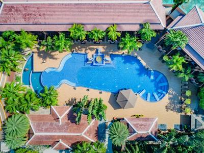 Vue aérienne d'une piscine d'hôtel tropical entourée de palmiers et de bâtiments.