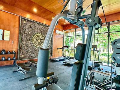 Salle de sport moderne avec haltères, équipements d'exercice et grandes fenêtres donnant sur la verdure.