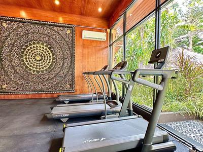 Salle de sport avec tapis roulants et grandes fenêtres donnant sur la verdure.