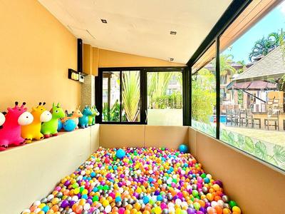 Hell erleuchteter Spielbereich mit Bällebad, bunten Sitzfiguren und großen Fenstern mit Gartenblick.