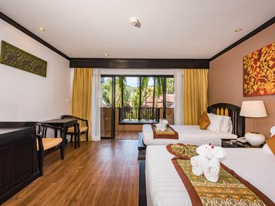 Helles Hotelzimmer mit zwei Betten, Holzboden, Schreibtisch und Blick auf einen Balkon mit Pflanzen.