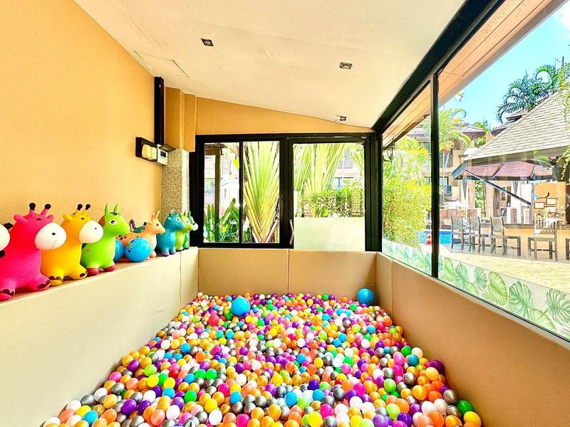 Hell erleuchteter Spielbereich mit Bällebad, bunten Sitzfiguren und großen Fenstern mit Gartenblick.