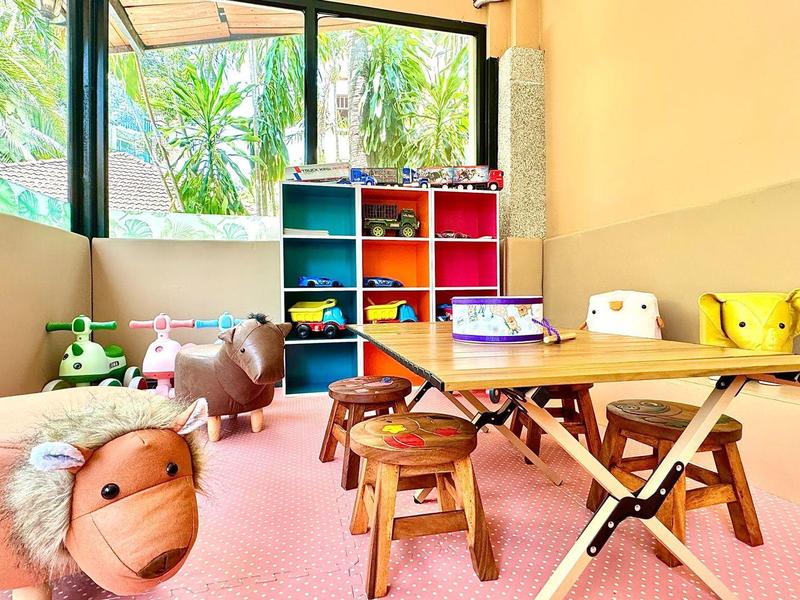 Bunter Kinderspielbereich mit Tischen, Stühlen, Spielzeug und großen Fenstern.