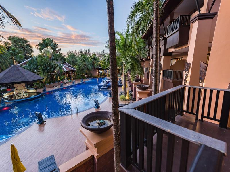 Blick von Balkon auf einen tropischen Poolbereich mit Palmen und Gästen im Wasser.