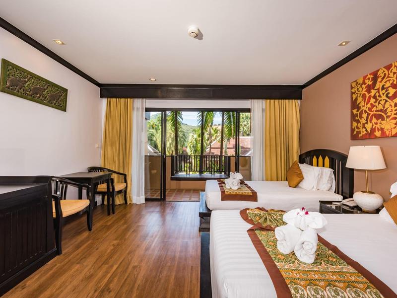 Helles Hotelzimmer mit zwei Betten, Holzboden, Schreibtisch und Blick auf einen Balkon mit Pflanzen.