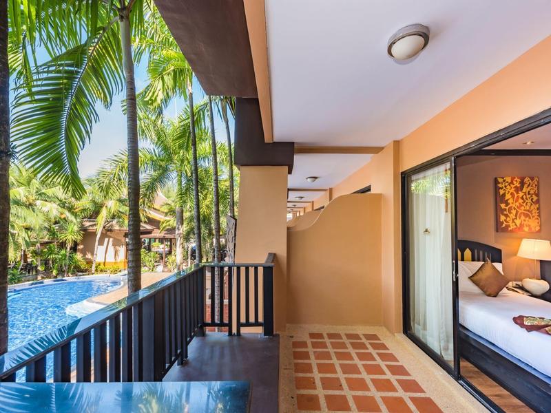 Balkon mit Blick auf einen Pool und tropische Pflanzen neben einem Hotelzimmer.