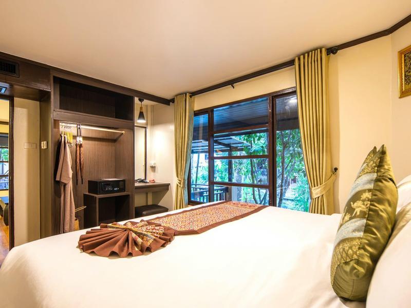 Gemütliches Hotelzimmer mit großem Bett, offenem Schrank und Blick auf die Natur durch große Fenster.