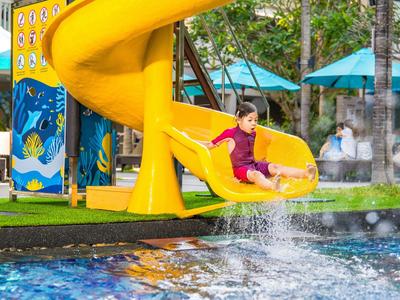 Dziecko zjeżdża ze żółtej spiralnej zjeżdżalni do hotelowego basenu