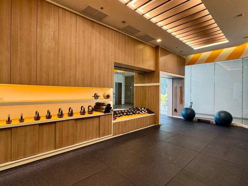 Nowoczesna siłownia z drewnianymi ścianami, hantlami i dużymi oknami wpuszczającymi naturalne światło.