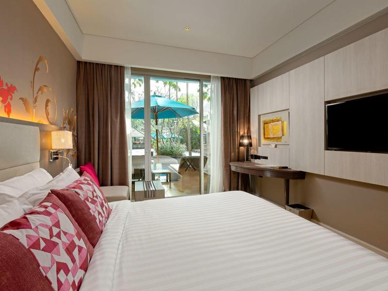 Nowoczesny pokój hotelowy z dużym łóżkiem, dekoracyjnymi poduszkami i widokiem na taras z parasolem.