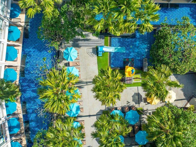 Widok z góry na basen hotelowy z leżakami i palmami.
