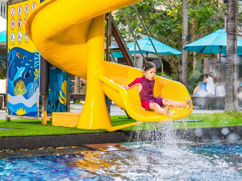 Dziecko zjeżdża ze żółtej spiralnej zjeżdżalni do hotelowego basenu