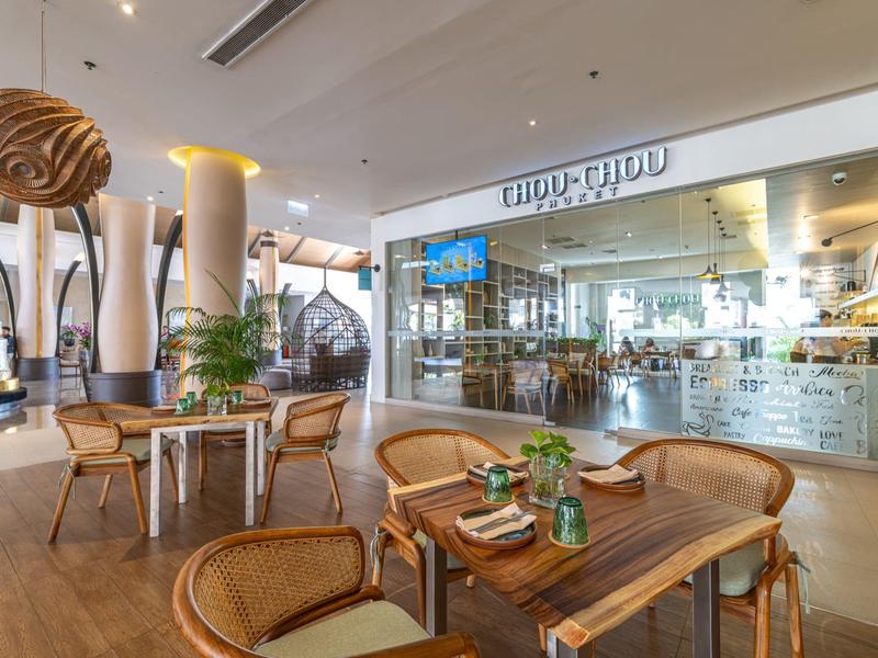 Nowoczesna część restauracyjna hotelu z drewnianymi meblami, roślinami i dużym oknem do kuchni.