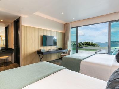 Moderne hotelkamer met twee bedden en uitzicht op zee en zwembad.