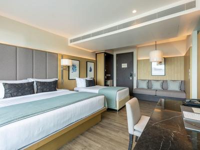 Modern hotelkamer met twee bedden, bureau en zithoek in neutrale tinten.