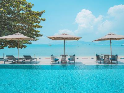 Pool mit Sonnenliegen und Schirmen am tropischen Strand mit blauem Himmel und Meer