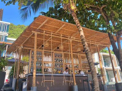 Buitenbar onder palmbomen met houten dak in een resort.