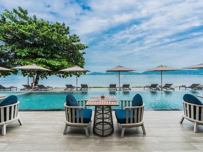 Moderne zwembadruimte met ligstoelen en parasols bij een strandhotel.