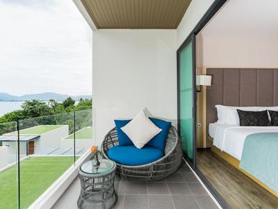 Balkon met stoel en tafel, uitzicht op tuin en zee, aangrenzende slaapkamer met moderne inrichting.