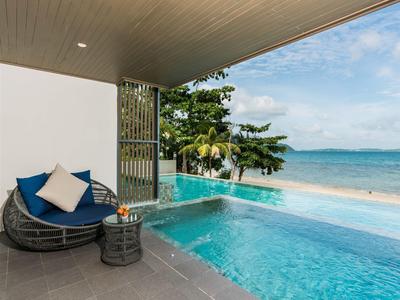 Een modern zwembad met uitzicht op zee en palmbomen, met een ronde ligstoel onder een overdekt gebied.