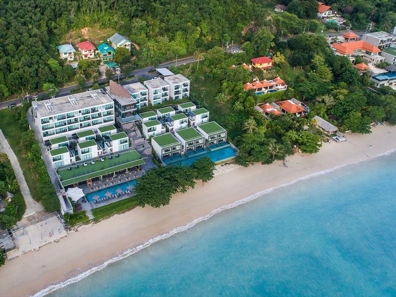 Luchtfoto van een resort aan het strand met meerdere gebouwen en zwembaden naast de zee.