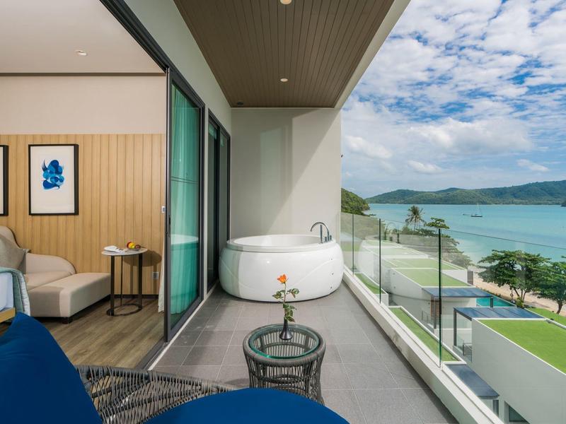 Hotelkamer met balkon, jacuzzi en zeezicht onder een heldere hemel.