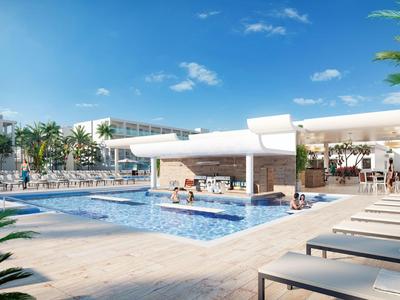 Moderní hotelový bazén s lehátky, palmami a jasně modrou oblohou.