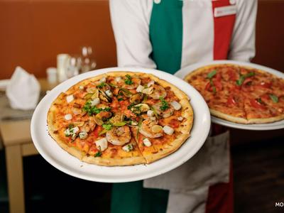 Cameriere che porta due piatti con pizze fresche in un ristorante.