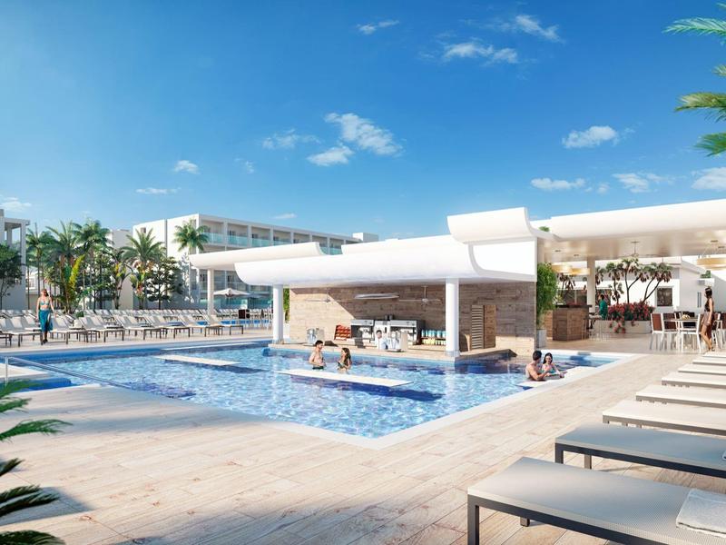 Moderní hotelový bazén s lehátky, palmami a jasně modrou oblohou.