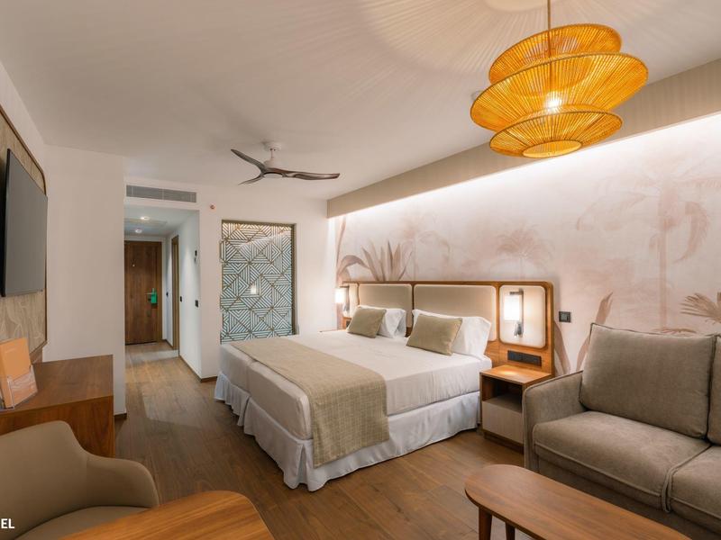 Moderní hotelový pokoj s manželskou postelí, pohovkou, dřevěnou podlahou a teplým osvětlením