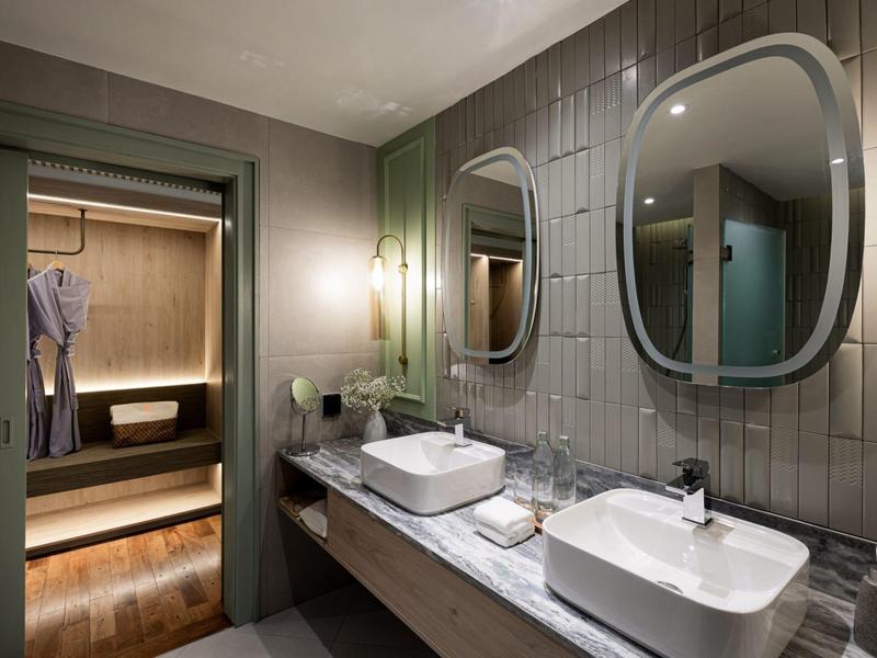 Modernes Badezimmer mit zwei Waschbecken und Blick in eine Sauna im Hintergrund.