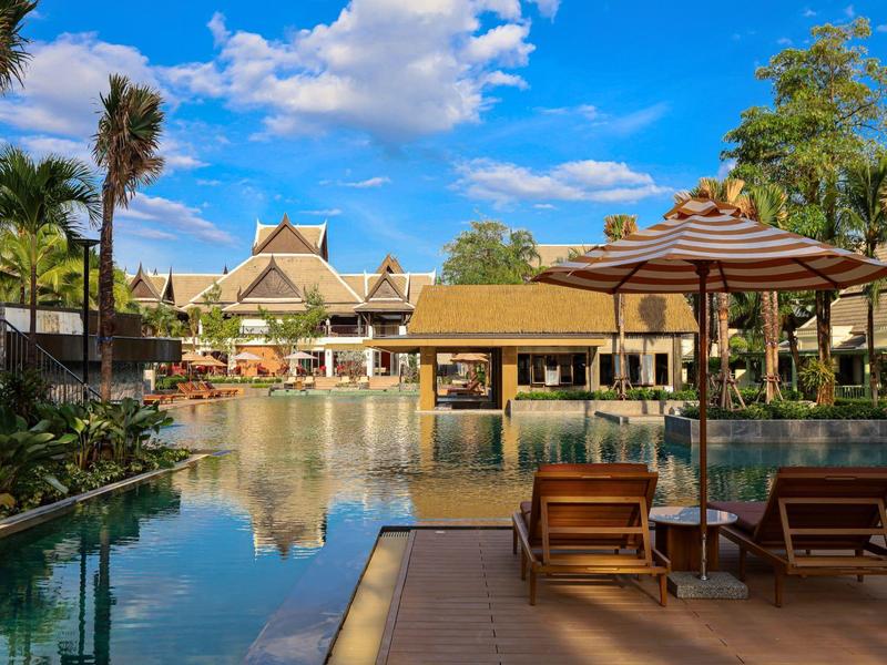 Luxuriöser Hotelpool mit Liegestühlen und Sonnenschirm unter blauem Himmel.