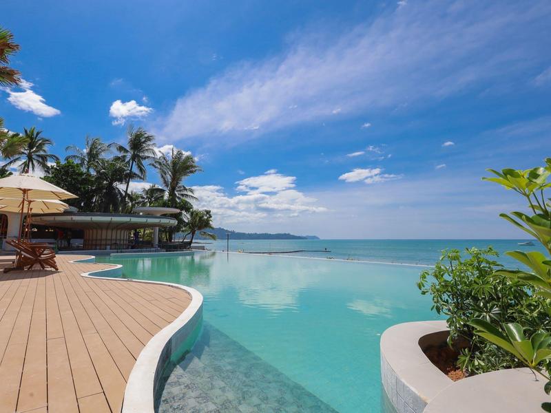 Infinity-Pool mit Holzdeck und tropischer Vegetation unter blauem Himmel am Meer