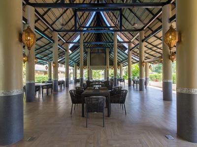 Area pranzo aperta con sedie e tavoli sotto un tetto alto con travi in legno.