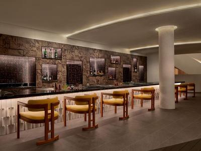 Nowoczesny bar hotelowy z podświetlanym ladą i żółtymi stołkami barowymi.