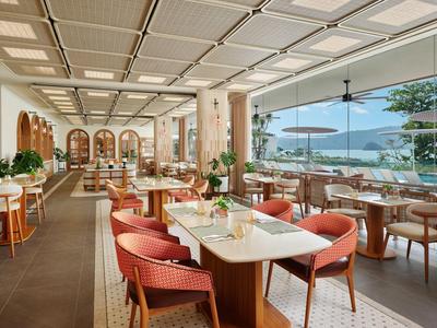 Ristorante luminoso e moderno con vista panoramica sul mare e tavoli e sedie ordinatamente disposti.