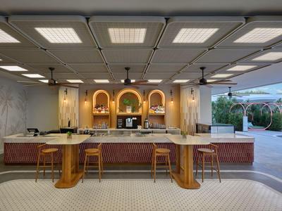 Nowoczesny bar hotelowy z drewnianymi i marmurowymi akcentami, stołkami i oświetleniem ambientowym.