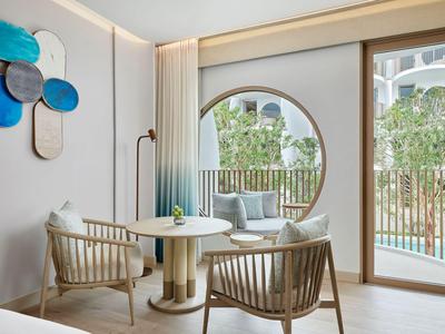 Nowoczesna część pokoju hotelowego z okrągłymi drewnianymi meblami i widokiem na taras z basenem.