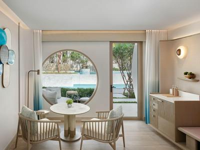 Nowoczesny pokój hotelowy z okrągłymi oknami, miejscem do siedzenia i widokiem na ogród.