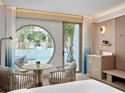 Nowoczesny pokój hotelowy z widokiem na basen przez duże okrągłe okno i eleganckie meble.