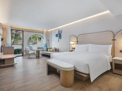 Nowoczesny pokój hotelowy z dużym łóżkiem, częścią wypoczynkową i balkonem z widokiem na zewnątrz.