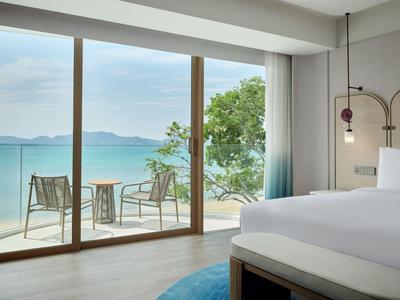 Nowoczesny pokój hotelowy z widokiem na morze i dostępem do tarasu z krzesłami i stołem.