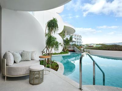 Nowoczesny balkon z białą sofą i roślinami obok basenu bez krawędzi z widokiem na wzgórza.