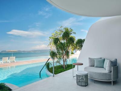 Area esterna moderna con piscina e zona salotto, vista sul mare e palme sotto un cielo azzurro.