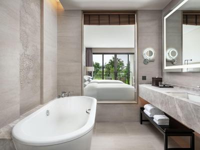 Salle de bain d'hôtel moderne avec baignoire autoportante, grand miroir et vue sur la chambre.