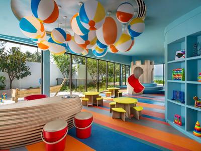 Salle de jeux enfantine avec balles colorées, tables rondes et mobilier bas dans un hôtel.