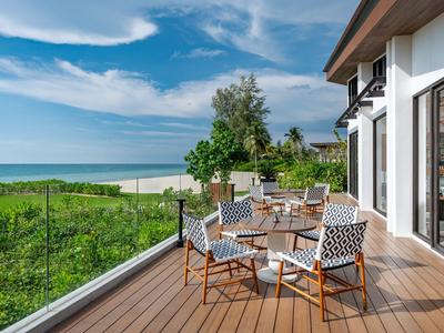 Balcon en bois avec table, vue sur un champ vert et la mer sous un ciel bleu.